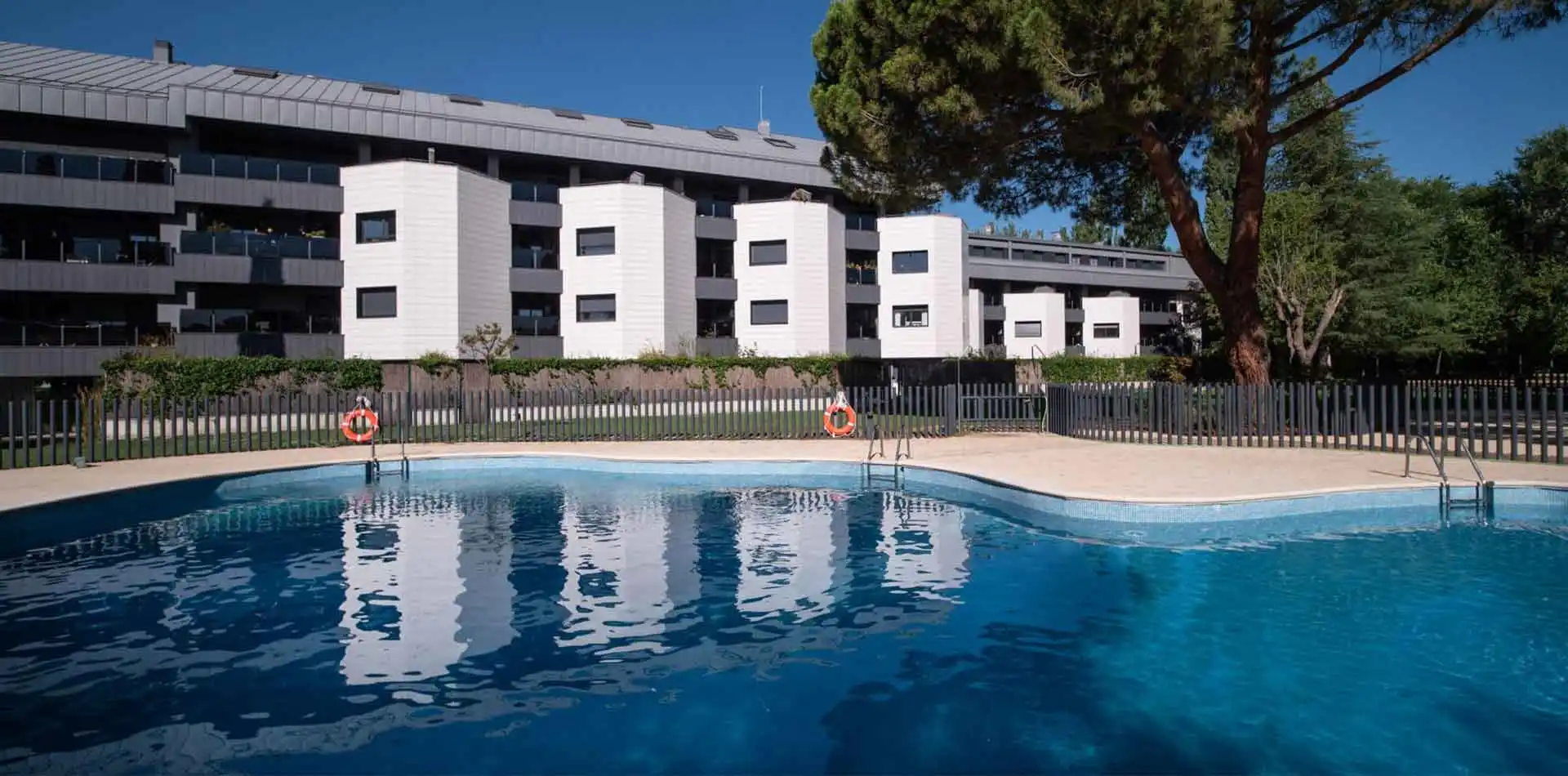 Piscina perfecta para refrescarte en verano en Lagos Park con fachada de fondo y viviendas con amplias terrazas, en jardín verde y cuidado con árboles.