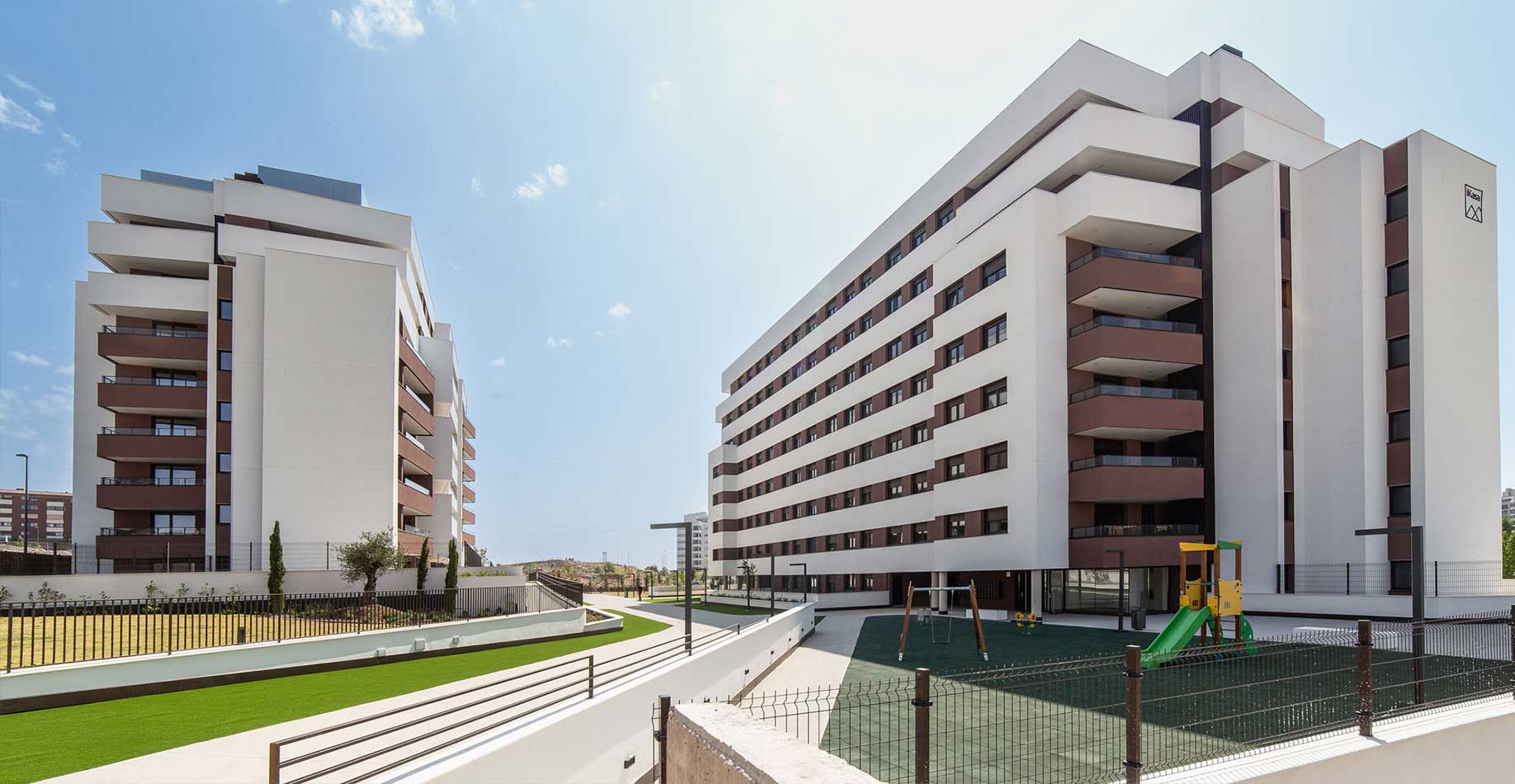 Zona de juegos infantiles y dos edificios de la promoción de viviendas iKasaClass Nuevo Tres Cantos